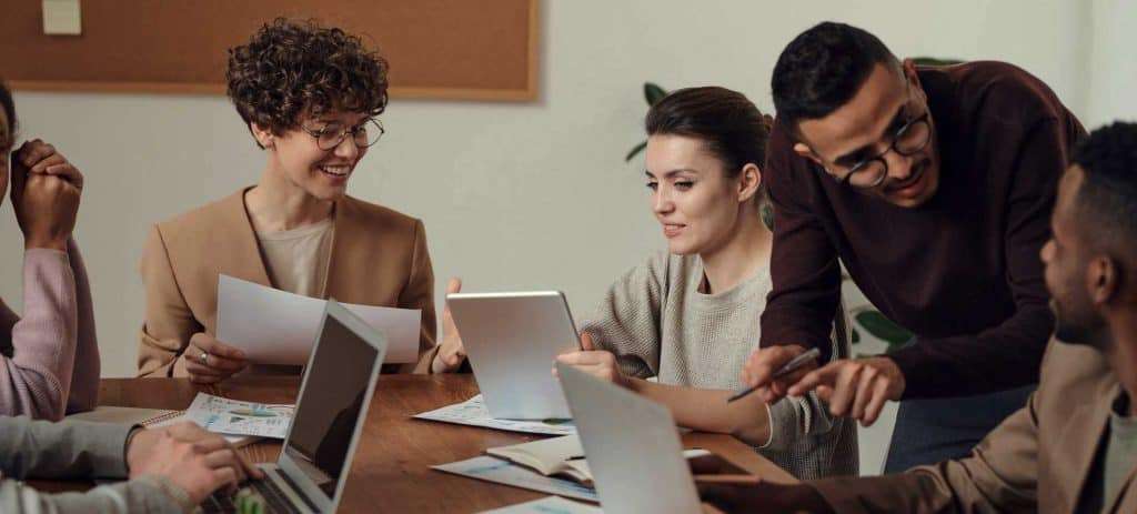 A diverse group of individuals engaged in a collaborative discussion around a table with digital devices