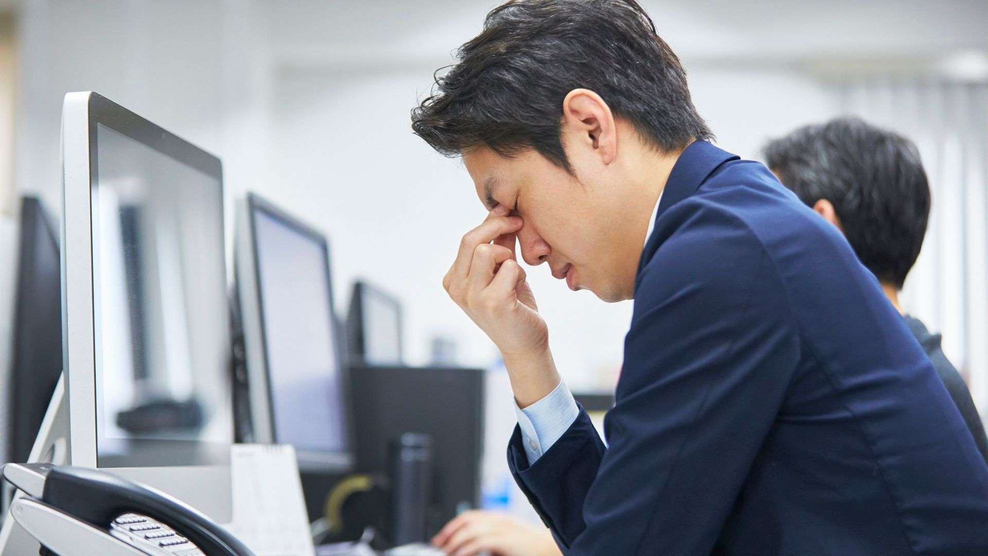 A person in an office environment showing signs of frustration or headache while working at a computer