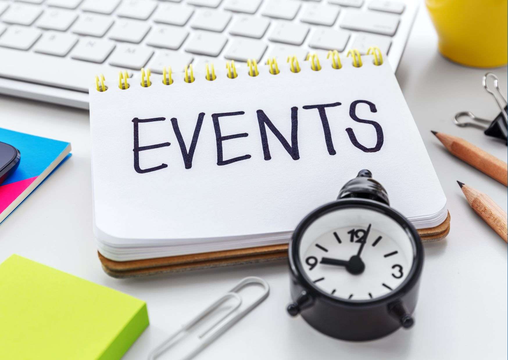 A notepad displaying the word 'EVENTS' next to a clock, indicating an organized approach to event management.